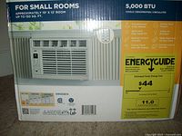 Box front showing product image, 5000 BTU cooling for small rooms approx 10' x 12' (150 sq. ft.), key features including remote control, LED display, energy saver, 3 fan speeds, and other operational modes. Energy guide shows estimated yearly cost of $44.