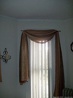 Photo showing one autumn colored window scarf draped over a curtain rod with vertical blinds in background.