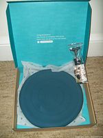 Photo of the blue inflatable balance disc inside an open box with the air pump and needle packaged next to it.