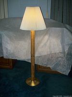 Full view of the bamboo and brass floor lamp with pleated shade showing lamp lit and entire structure.