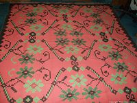 Full view of large textile rug with geometric floral and vine patterns in green, brown, and black on coral background