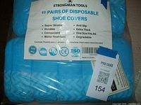 Blue disposable shoe covers in original packaging with label showing brand Strongman Tools, quantity 60 pairs, and usage features.