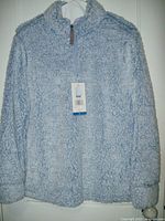 Front view of periwinkle blue fleece pullover tunic hanging on hanger, showing texture and half zipper front with tag attached.