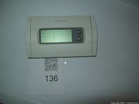 Honeywell digital thermostat mounted on wall showing front LCD display and two control buttons