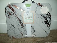 Front of lap desk showing marble design hard top with integrated drink holder and attached carry handle with packaging labels