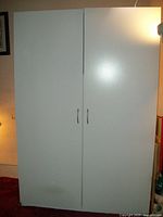 Closed white two-door wardrobe closet shown assembled in room.