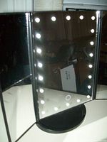 Front view of battery operated makeup mirror with LED lights around main mirror, displayed with doors open revealing additional mirrors inside the doors, circular base