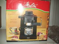 Front view of Melitta 4 cup espresso cappuccino maker in original red and yellow box with espresso machine image and coffee cup on front.