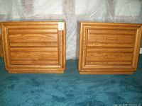 Front view of two solid oak nightstands with flat tops and two drawers each, medium wood finish, placed side-by-side on blue carpet.