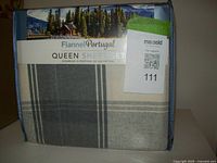 Packaged queen size flannel sheet set in original plastic wrapping showing gray and white plaid pattern and label with cabin and pine trees.