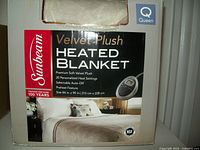 Front packaging view of the Sunbeam Velvet Plush Heated Blanket showing brand, key features, image of controller, and queen size label.