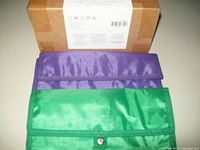 Two soft fabric pencil cases, purple and green, displayed flat showing flap with snap button closures and rectangular shape.