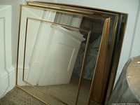 Three gold-framed square Art-Deco styled mirrors stacked together leaning against a white door, showing gold outer frames and inner thin gold border details. Mirrors are clean and reflective with no visible cracks.