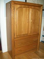 Front view of solid oak armoire with two doors and two bottom drawers, showing wood finish and overall condition.