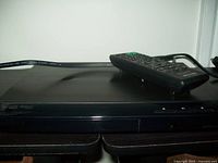 Sony DVD player shown with remote control resting on top, front panel clearly visible with disc tray and buttons.