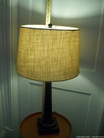 Full view of the table lamp showing the base and burlap shade, light on, highlighting the texture of the shade and overall shape.