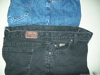 Top view of the black and navy blue Lee jeans laid flat showing front pockets and waistband, highlighting the leather Lee brand patch on black jeans