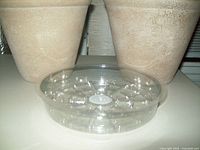 Two beige 8-inch planters and one clear plastic drip tray in front, showing texture and shape