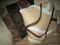 Two brown throw pillows with abstract circular designs and one beige-based pillow with brown and white abstract patterns resting on a bed.