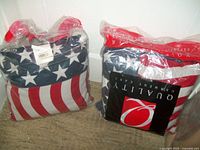Two USA flag throw pillows in plastic bags with retail tag visible showing brand and product details.