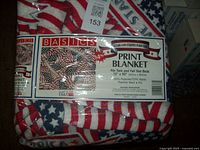Photo showing the blanket in original packaging with label indicating brand Basic Editions, material composition, size 72" X 90", and patriotic American flag print.