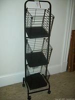 Front view of the black metal kitchen cart showing three evenly spaced wire baskets and four wheels.