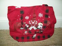 Full view of red tote bag showing Mickey and Minnie Mouse holding candy canes forming a heart, snowflakes, and black plaid trim and handles.