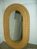 Front view of the oval mirror showing the tightly woven wicker frame and reflective glass surface.