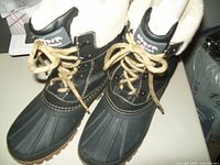 Front and top view of the pair of black Cougar storm boots with fleece lining, showing the beige laces and fleece interior, rubber lower section, and stitching details.