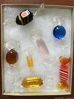 Top-down view of all seven Murano glass candy figurines arranged in a lined box with white padding.