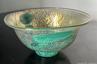 Side angle view of green aventurine art glass bowl showing the textured speckled silver pattern and signature color inclusions on black surface.