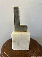 Front view of bronzed metal letter 'L' on alabaster base showing texture and finish.