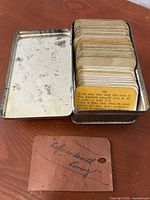 Tin box opened to reveal neatly stacked scripture parable cards inside, with handwritten note card reading "Life is best living".