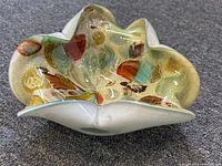 Oblique angled view of the Murano art glass bowl showing the colorful interior pattern and white exterior with a flower-shaped, wavy rim.