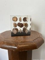 Clear Lucite cube paperweight with 36 pennies suspended inside, showing different coin faces and edges arranged in a grid pattern.