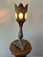 Front view of the glowing lamp lit, showing metal filigree and glowing glass prisms in tulip-shaped shade.