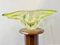 Side view of large translucent chartreuse green glass bowl with flowing organic design on a wooden stand.