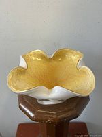 Front angle view of the golden-yellow aventurine glass bowl with ruffled edges, showing the textured inner glass pattern and smooth white outer surface.