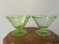Pair of green Vaseline glass optic ribbed sherbet coupe footed bowls shown side by side on wooden surface.