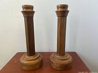 Pair of solid wood Arts & Crafts style candlesticks with octagonal turned stems placed on wooden surface against plain wall.