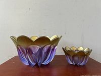 Front and side view of two deep purple and gold glass bowls with scalloped edges on a wooden surface.