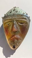 Close-up front view of textured art glass mask paperweight showing face details and colors.