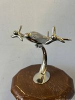 Front and top view of the silvered metal airplane statue with two propellers mounted on a curved stand and oval base.