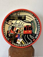 Front view of round drinks serving tray with illustrated London Underground platform and tube train scene in cartoon style.
