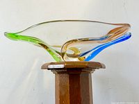 Side view of the colorful art glass bowl on a wooden stool showing the swirling colors