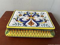 Top view of elongated rectangular pottery box showing fleur-de-lys floral design with detailed hand painting in blue, orange, green, and yellow.
