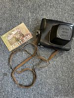 Zenit EM instruction booklet next to the black leather carrying case with strap on carpeted floor.