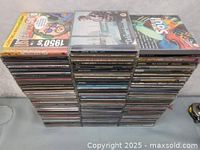 Stack of 100 music CDs showing the top few cases with various cover artworks.