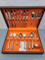 Full open case showing knives, forks, spoons and serving pieces in orange lining.