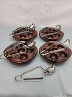 Four brown glazed ceramic escargot/mushroom plates and four stainless steel snail tongs arranged in a group.